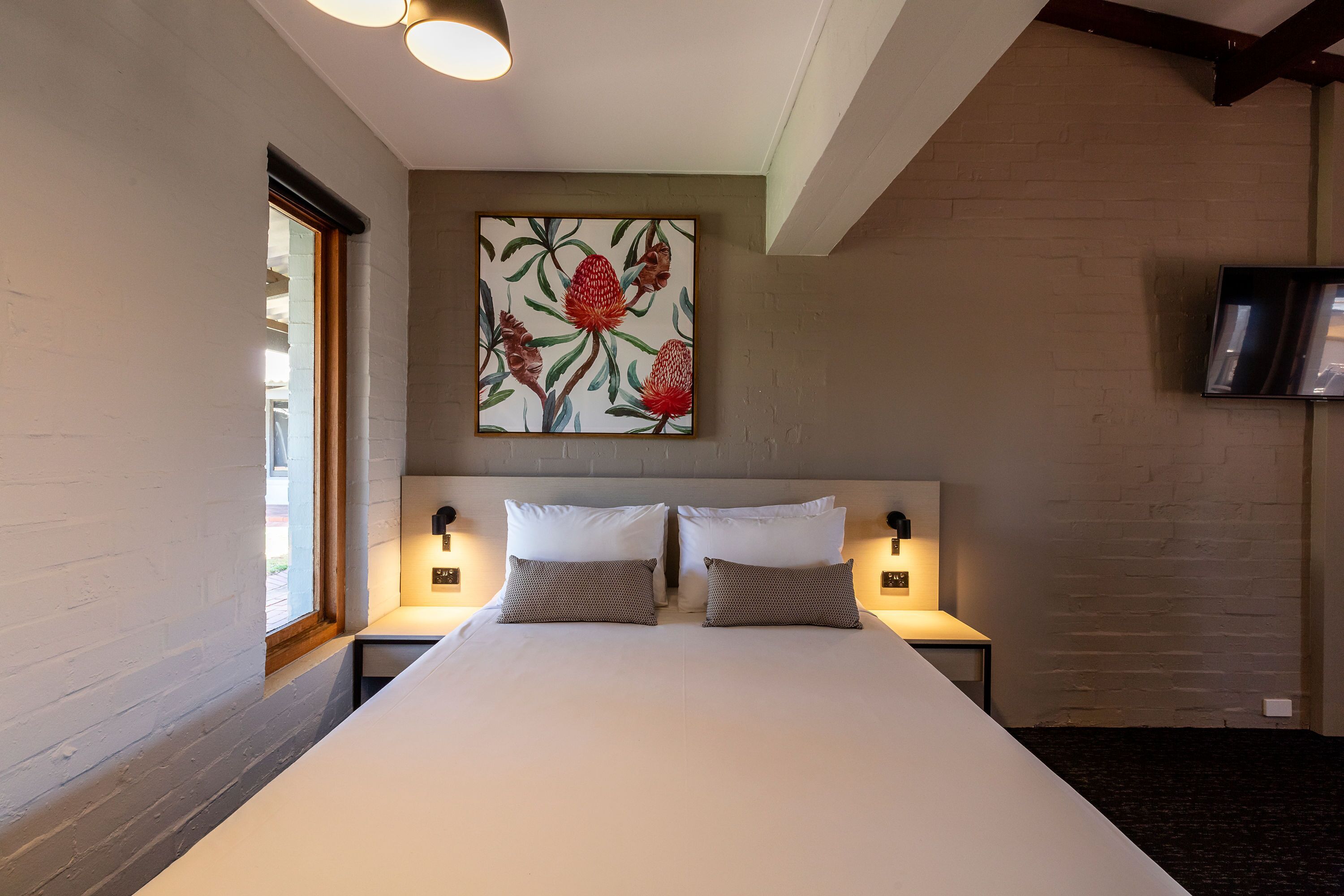 A hotel room with a large bed, two bedside tables with lamps, a wall-mounted TV, and a window with a view.