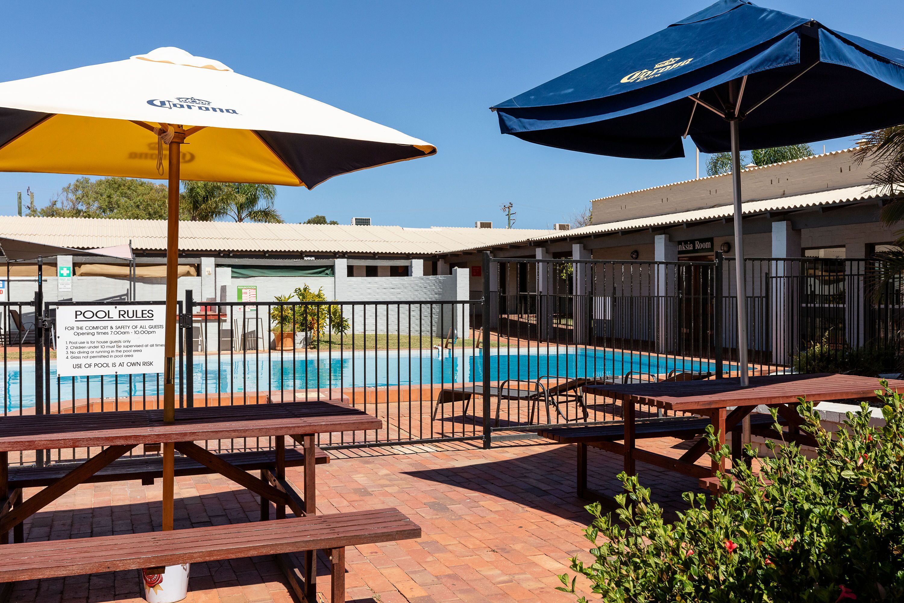 A pool area with umbrellas, a sign indicating pool rules, and a poolside seating area.