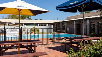 Zona de piscina con sombrillas, un cartel con las normas de la piscina y un área de descanso junto a la piscina.