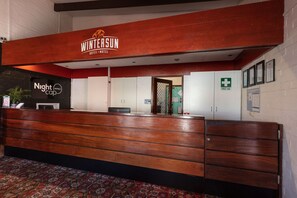 A reception desk with a wooden finish, a sign for Wintersun Hotel, a Nightcap sign, and a first aid sign.