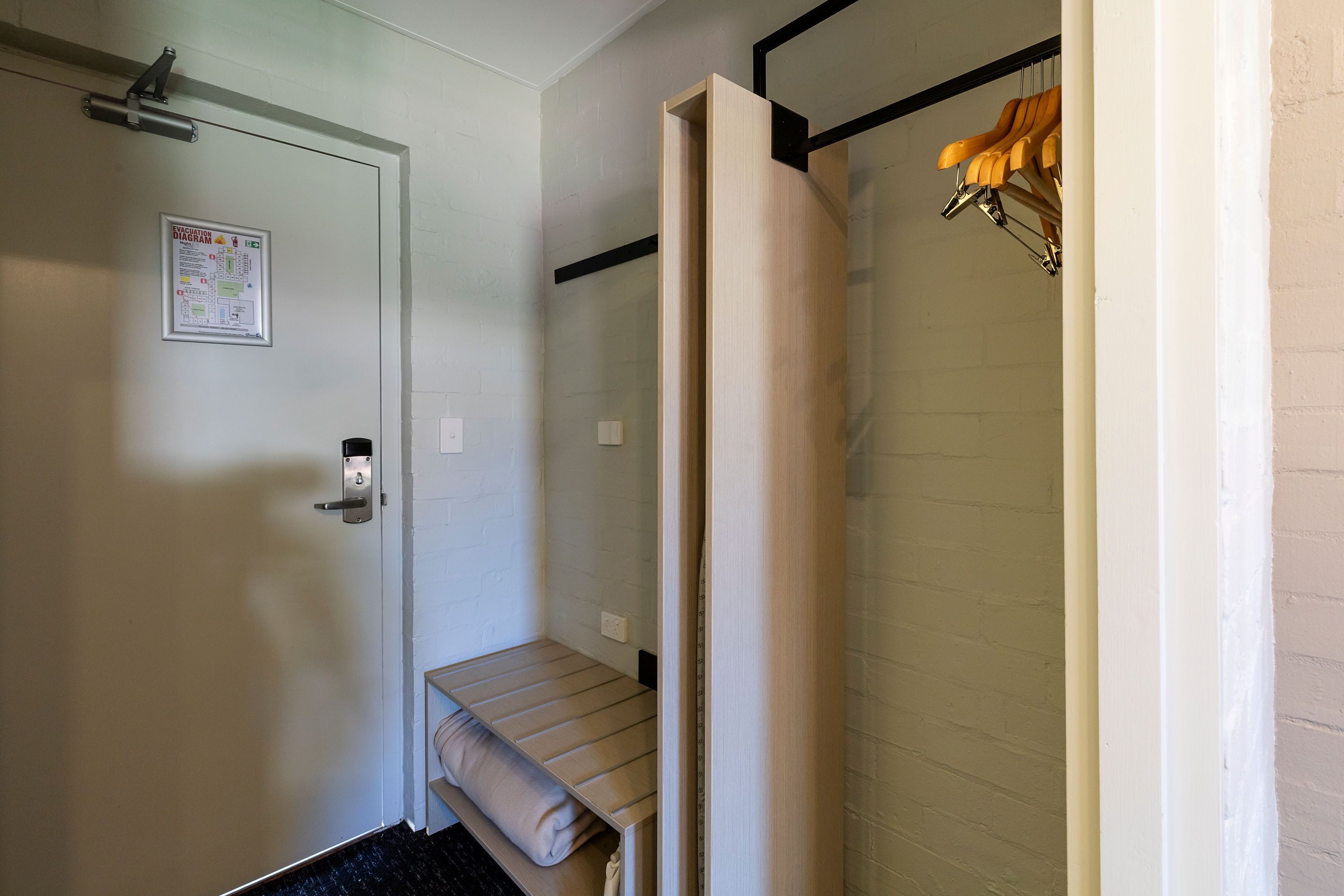 Um quarto pequeno com uma cama, uma porta com puxador, uma toalha e uma cadeira de madeira pendurada.