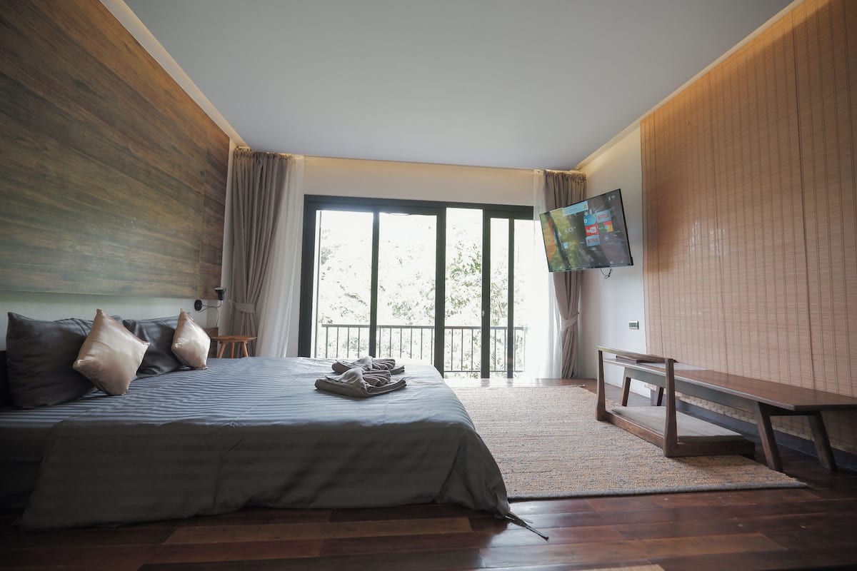 A bedroom with a bed, a TV, a bench, and a view of the outdoors.