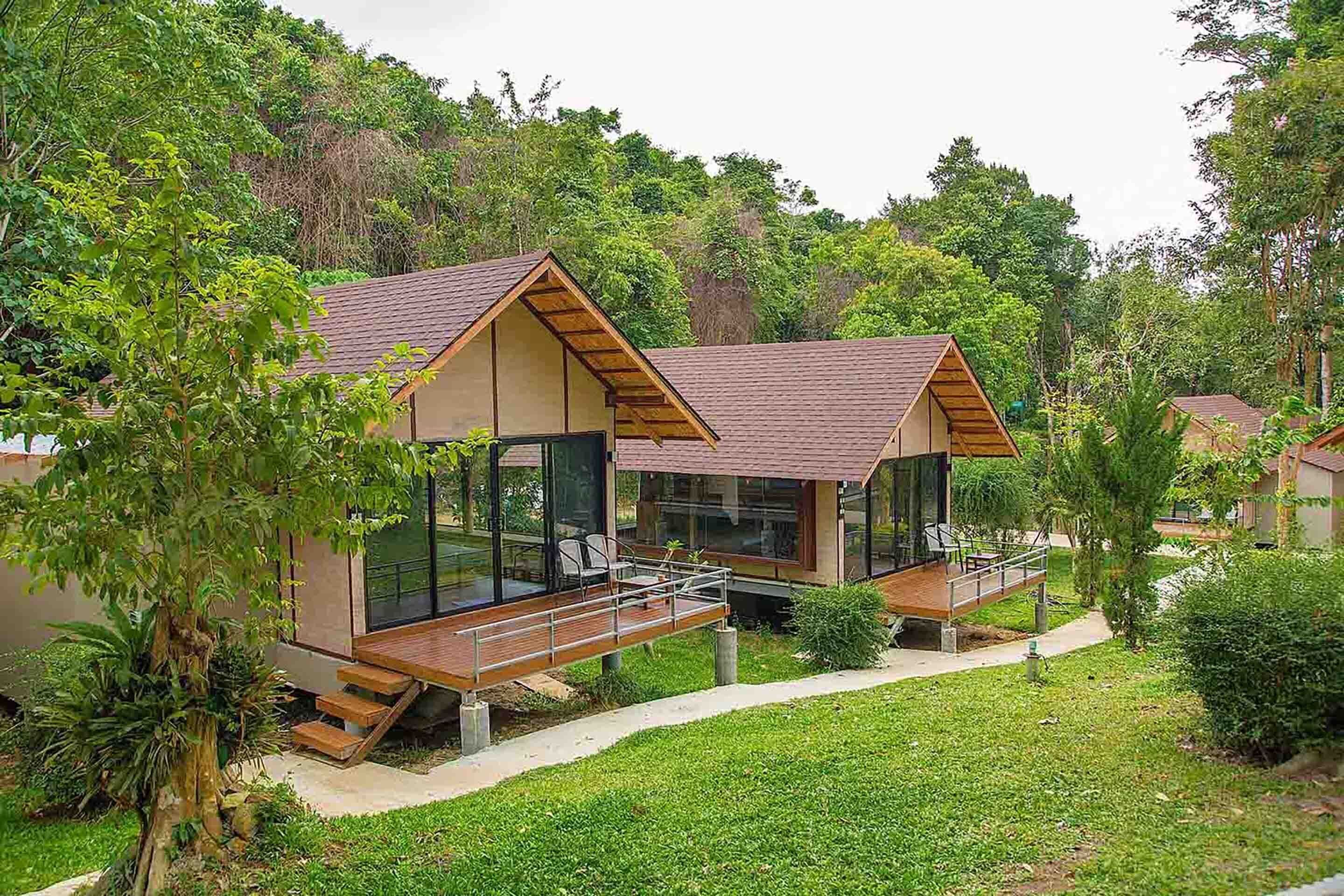 Ein modernes Bungalow mit Glasbalkon, umgeben von üppiger Vegetation.