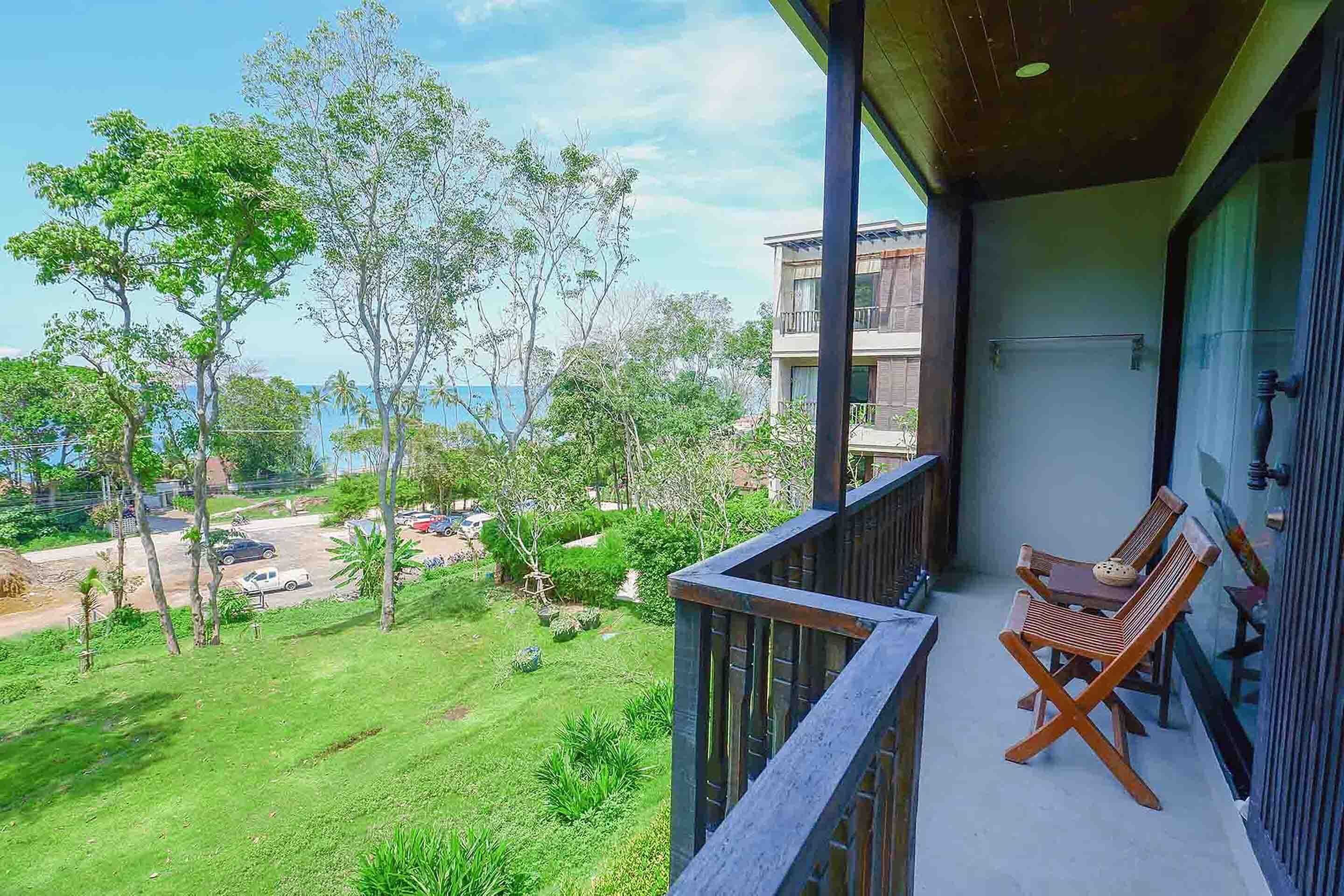 Een balkon met uitzicht op een grasveld en bomen, een tafel met stoelen, en een gebouw op de achtergrond.