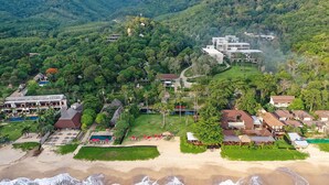 Vista aerea di una località balneare con diversi edifici, una spiaggia e vegetazione rigogliosa.