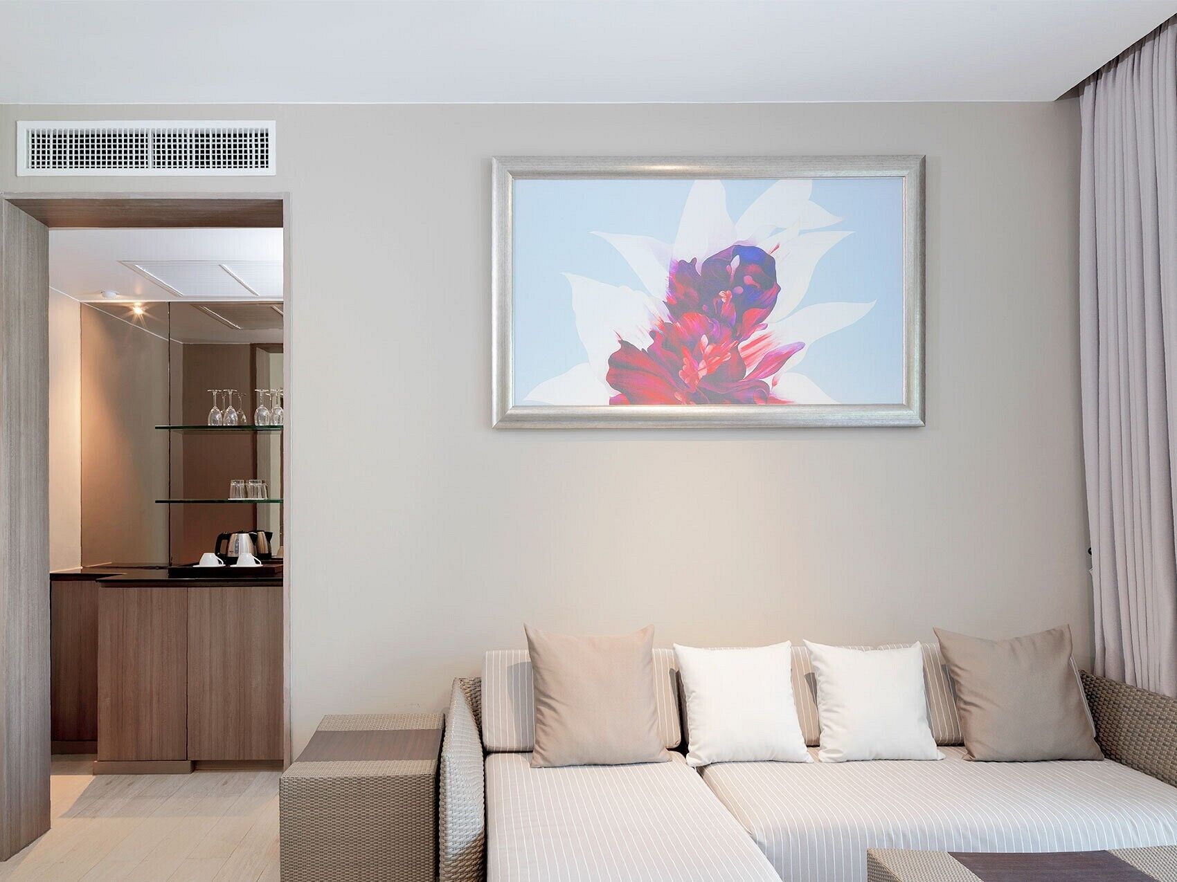 A modern hotel room with a sofa bed, a framed abstract painting, and a kitchenette area.