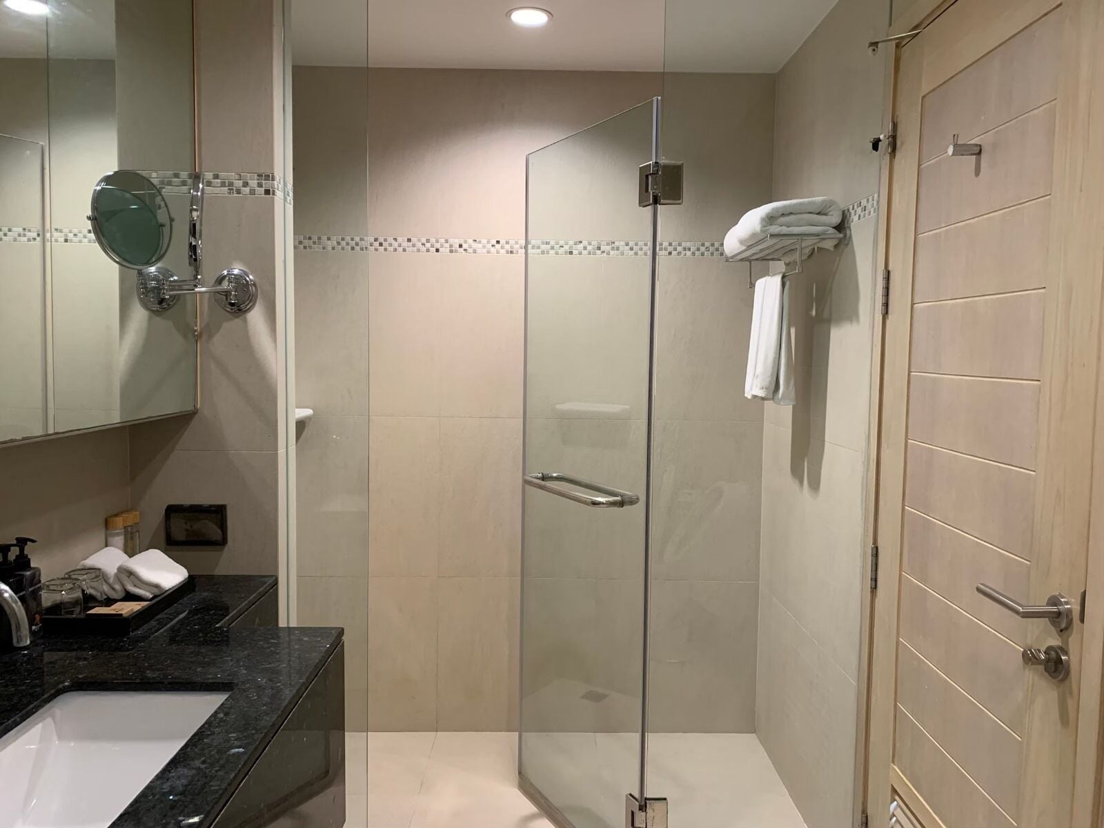 Une salle de bain moderne avec une douche à parois de verre, un lavabo doté d’un plan de travail noir et une porte en bois.