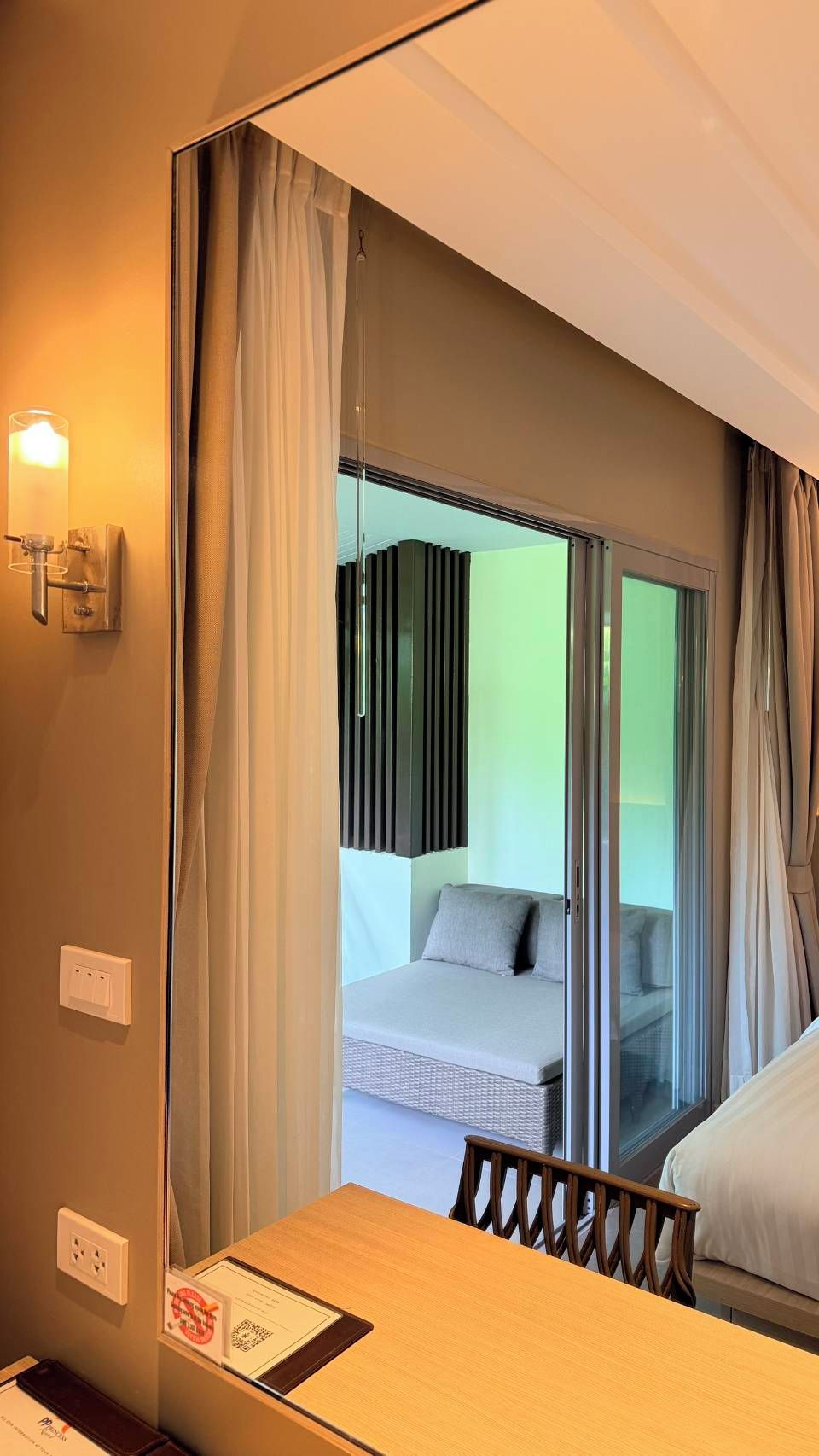 A hotel room with a bed, a table, a chair, and a view through a glass door.
