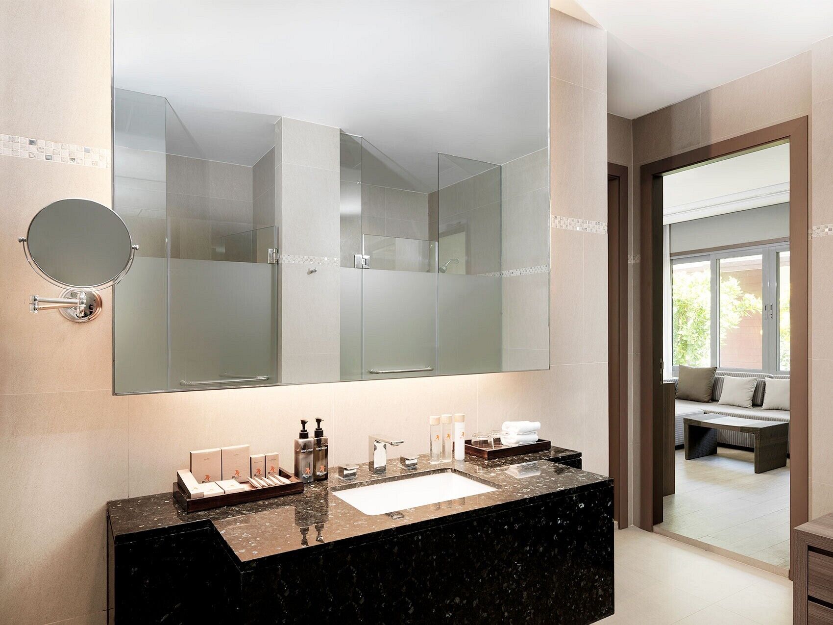 A modern bathroom with a large mirror, a black marble sink, and a glass shower enclosure.