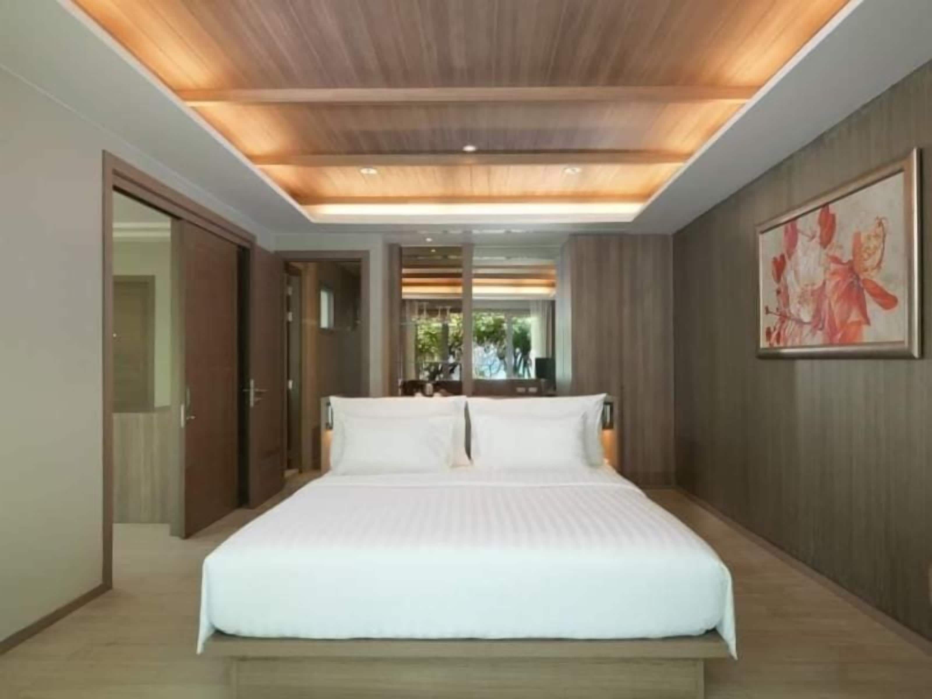 A modern bedroom with a large bed, wooden ceiling, and a framed painting on the wall.