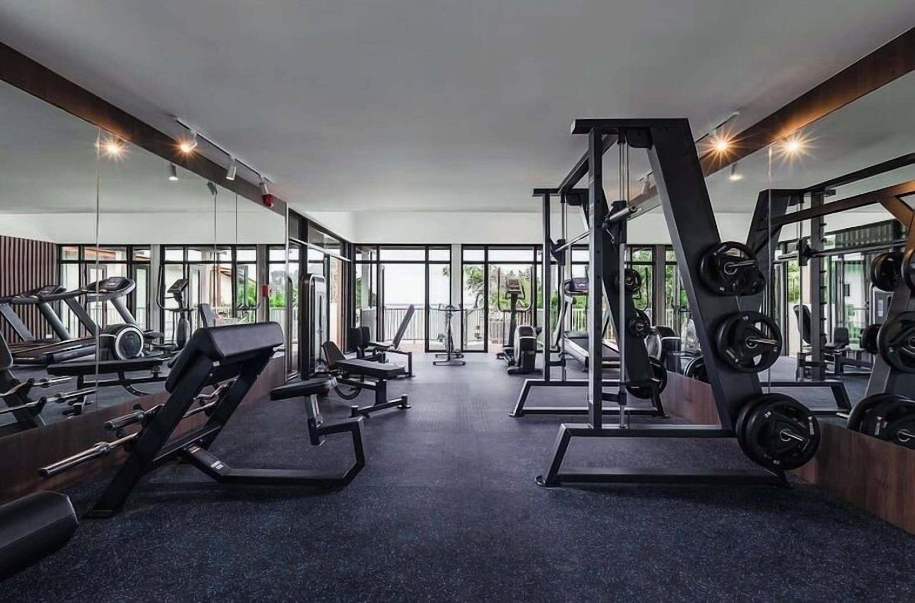 Un gimnasio con equipo cardiovascular, máquinas de pesas y ventanas amplias.