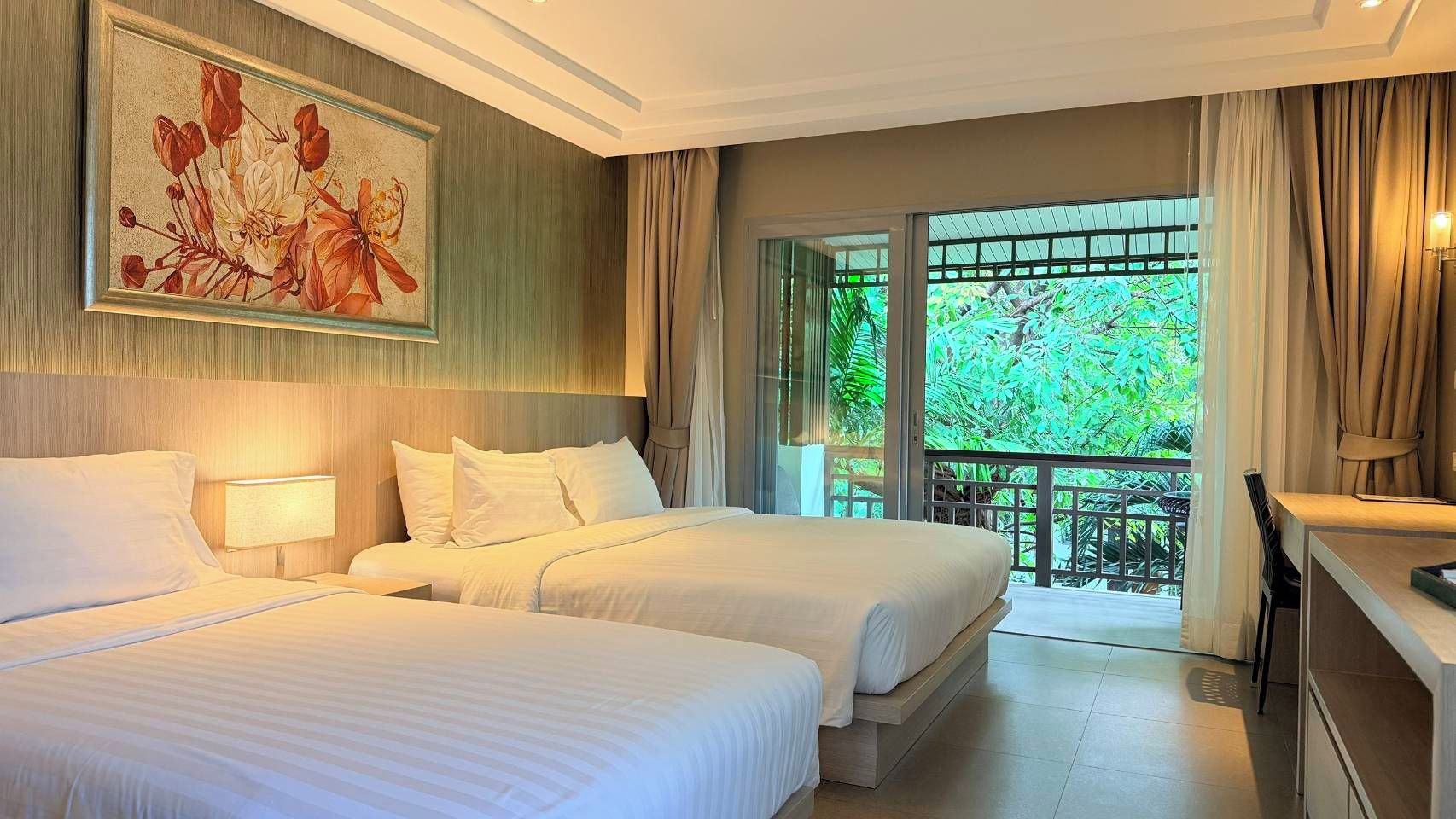 Habitación de hotel con dos camas, un cuadro en la pared, un balcón con vistas a zonas verdes y un escritorio con lámpara.