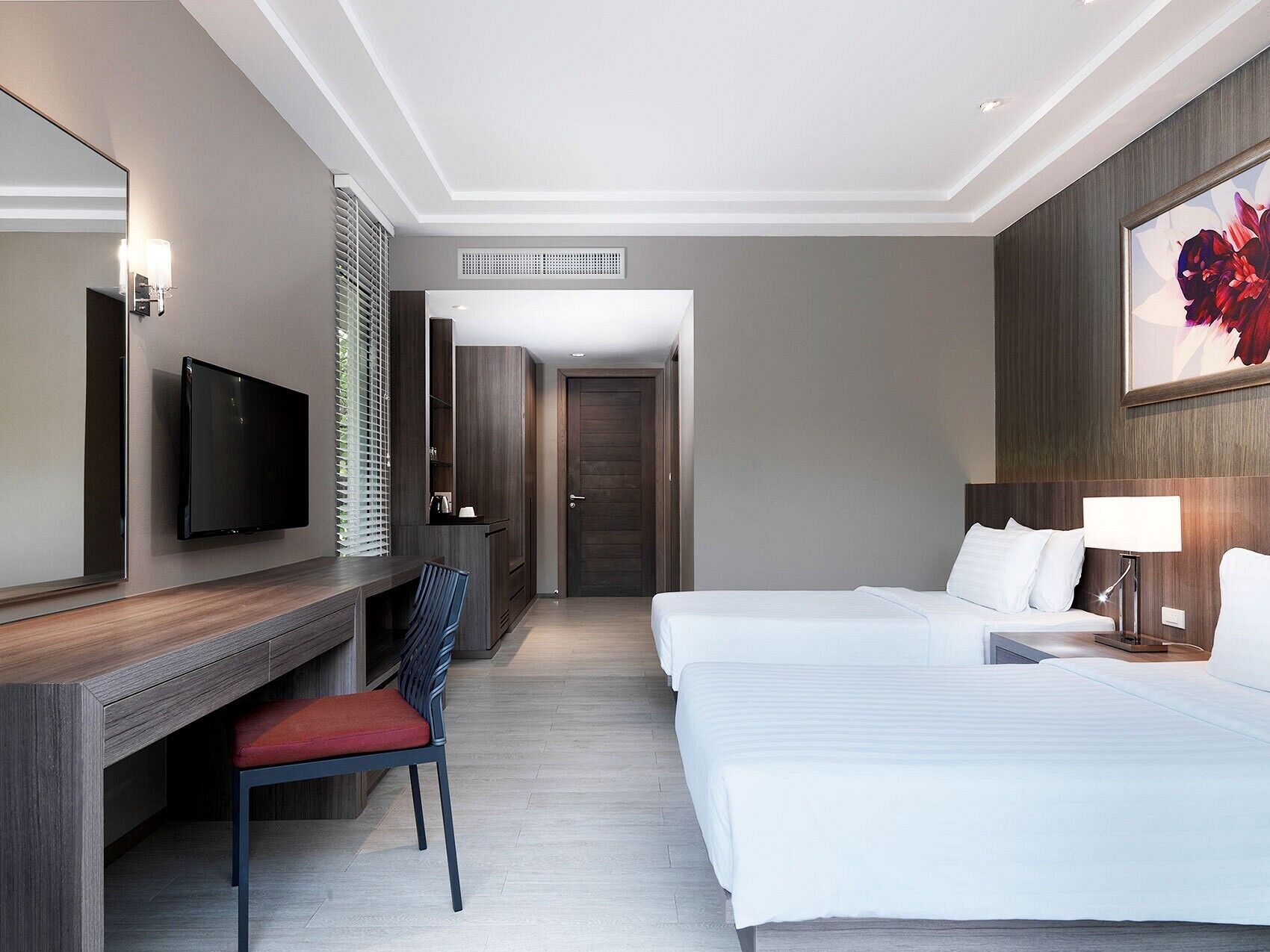 A hotel room with a TV, a desk, a chair, two beds, and a painting on the wall.