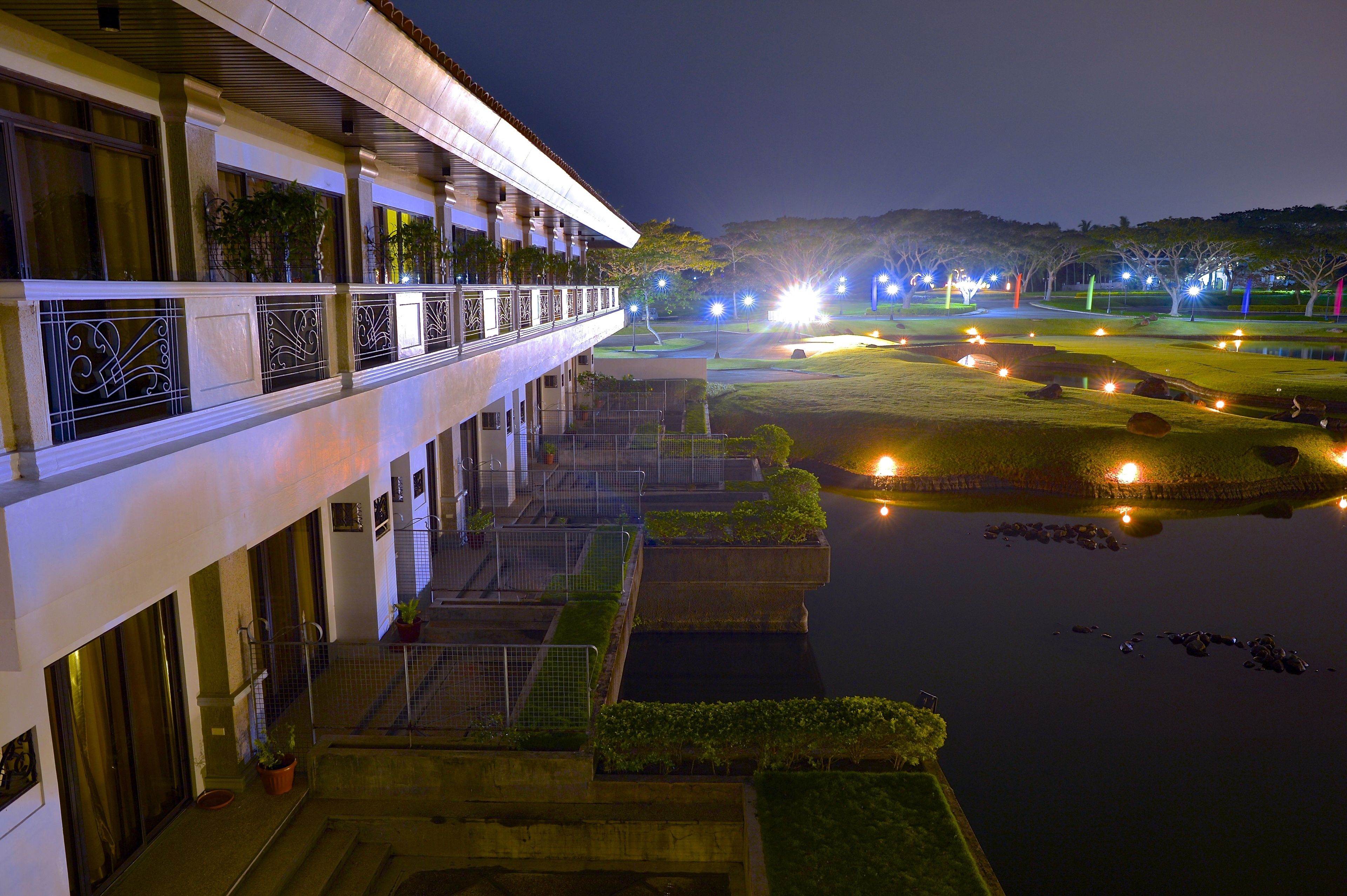 A hotel with a balcony overlooking a landscaped garden and a pond.