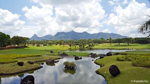 A golf course with a pond, palm trees, and mountains in the background. - The Suites at Mount Malarayat (Lipa)