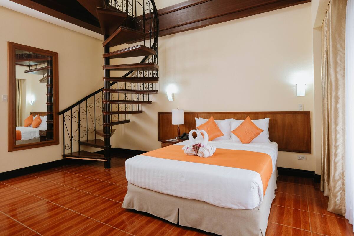A hotel room with a wooden staircase, a large bed with an orange bedspread, and a headboard with two orange pillows.