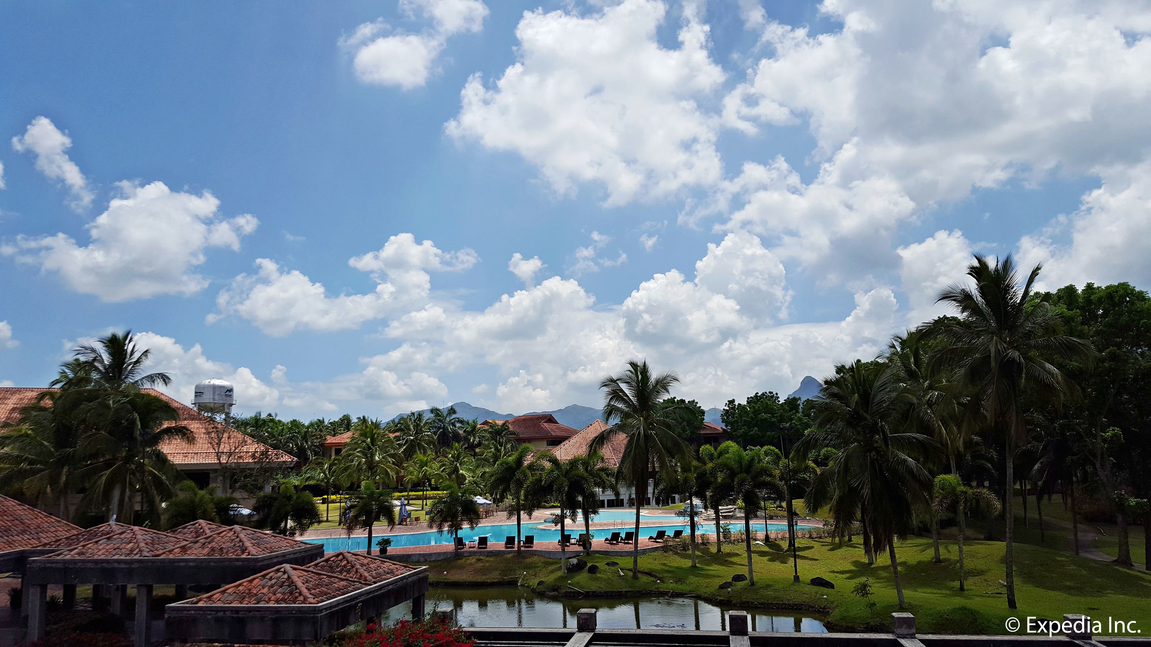 Um resort com piscina, palmeiras e montanhas ao fundo.
