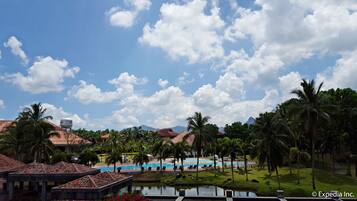 Um resort com piscina, palmeiras e montanhas ao fundo.