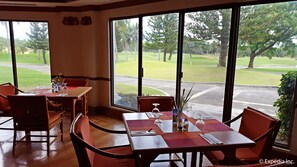 A dining area with tables and chairs, large windows offering a view of a golf course. - The Suites at Mount Malarayat (Lipa)