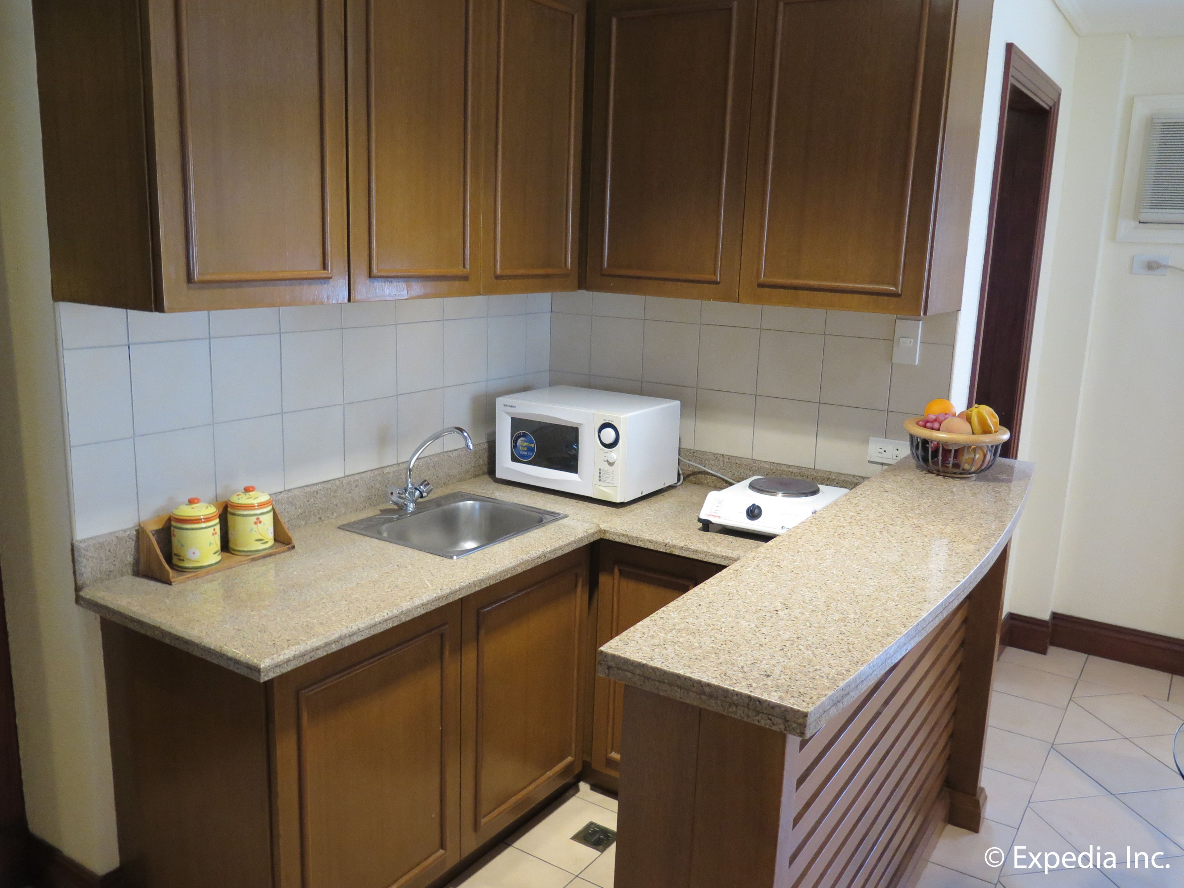 A kitchen with wooden cabinets, a stainless steel sink, a microwave, a stove, and a fruit bowl on the counter.