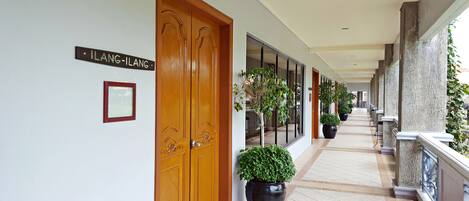 A corridor with wooden doors, potted plants, and a sign reading "LANG-ILANG".