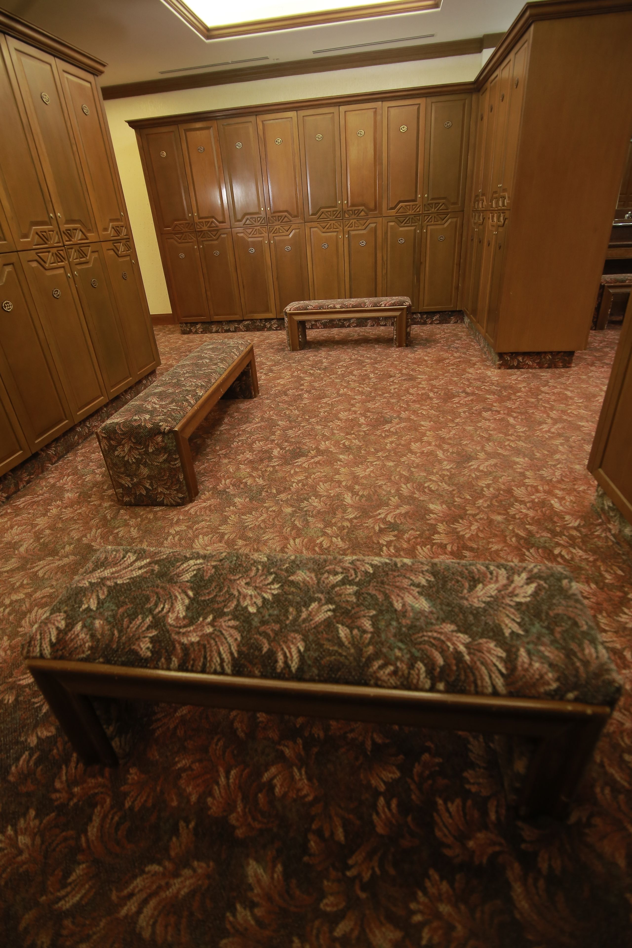 A room with a patterned carpet, wooden cabinets, and a bench.