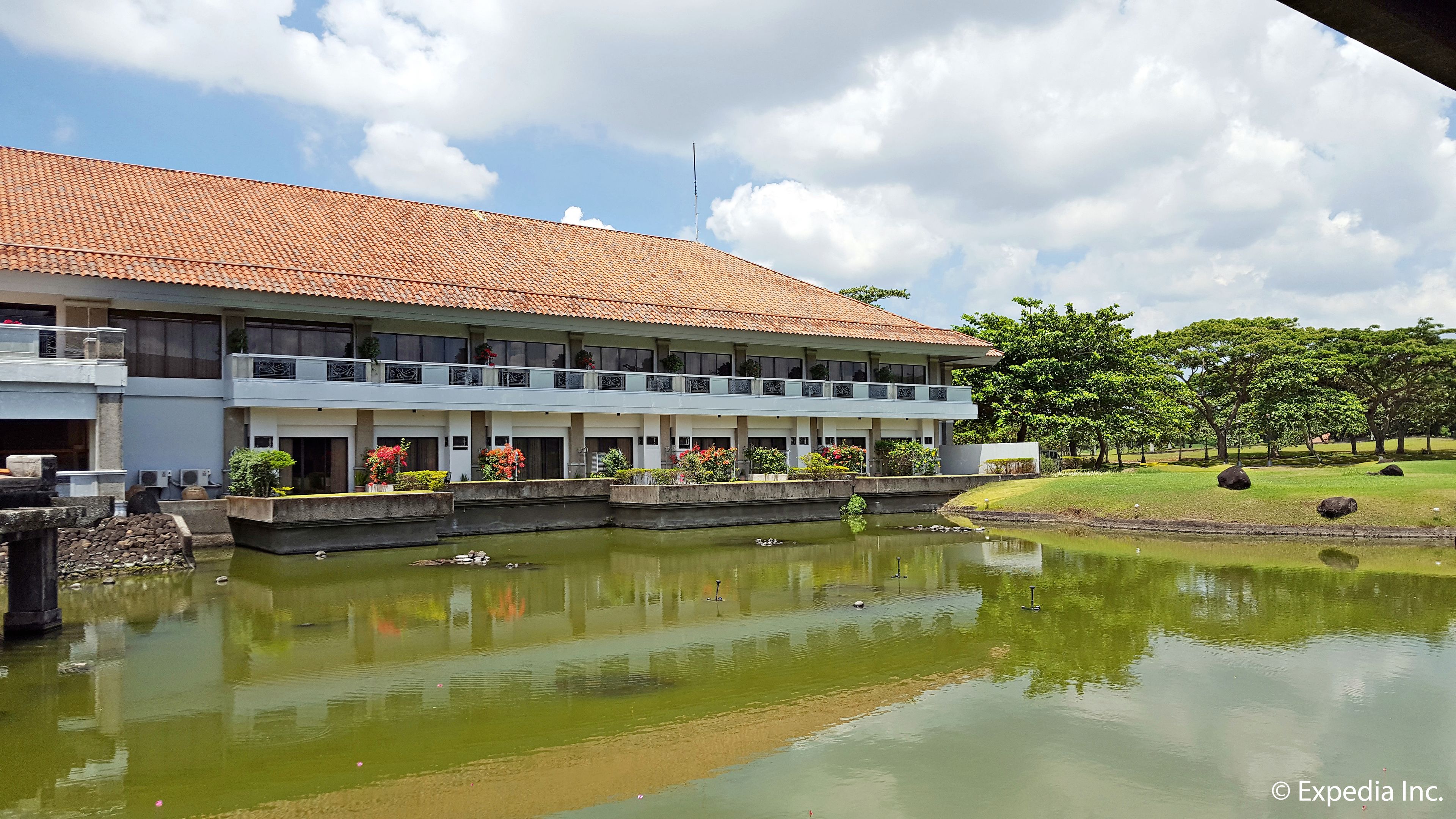 A hotel with a tiled roof, a courtyard with a pond, and a garden with trees.