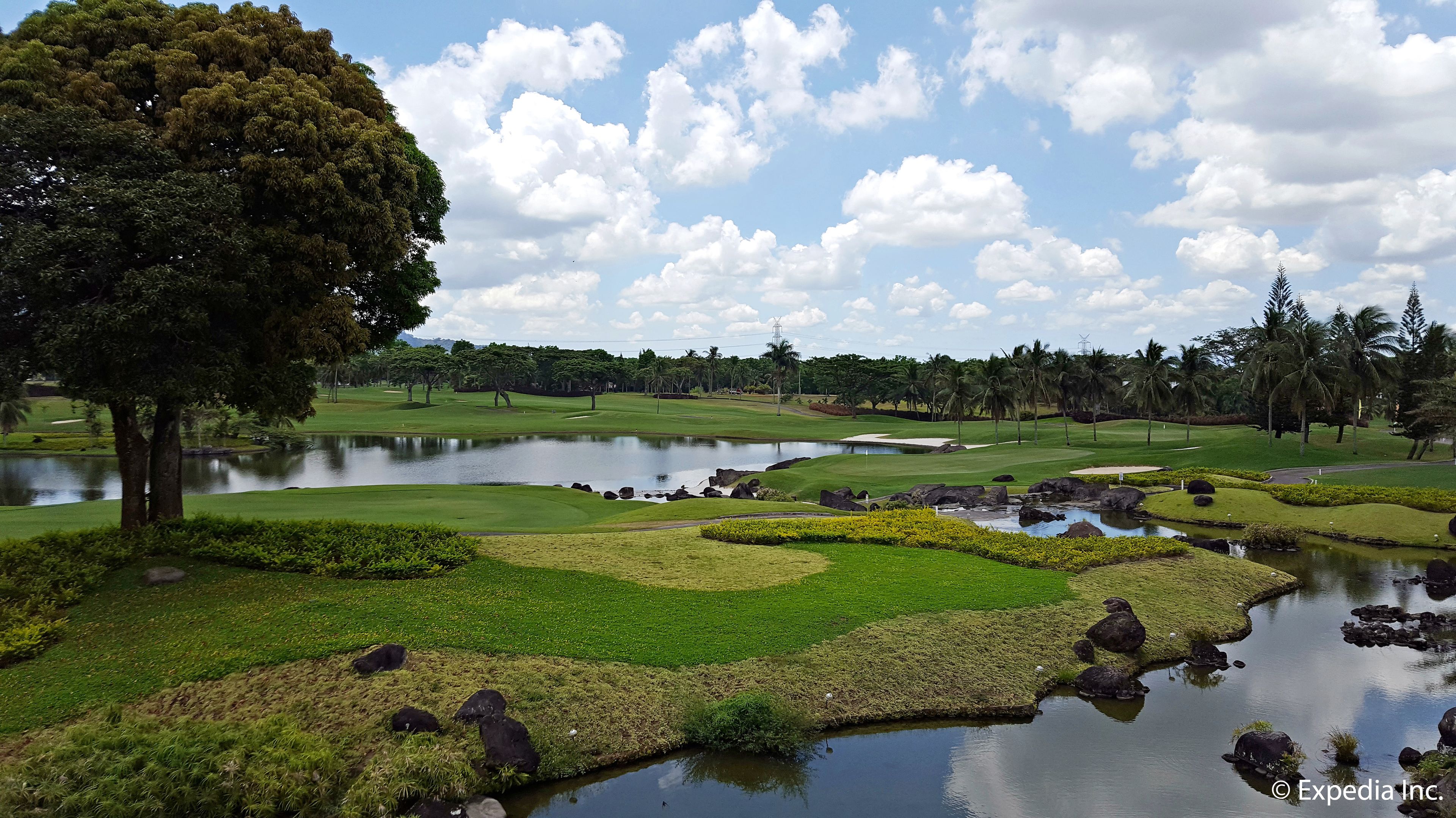 Un campo de golf con estanques, árboles y cielo despejado.