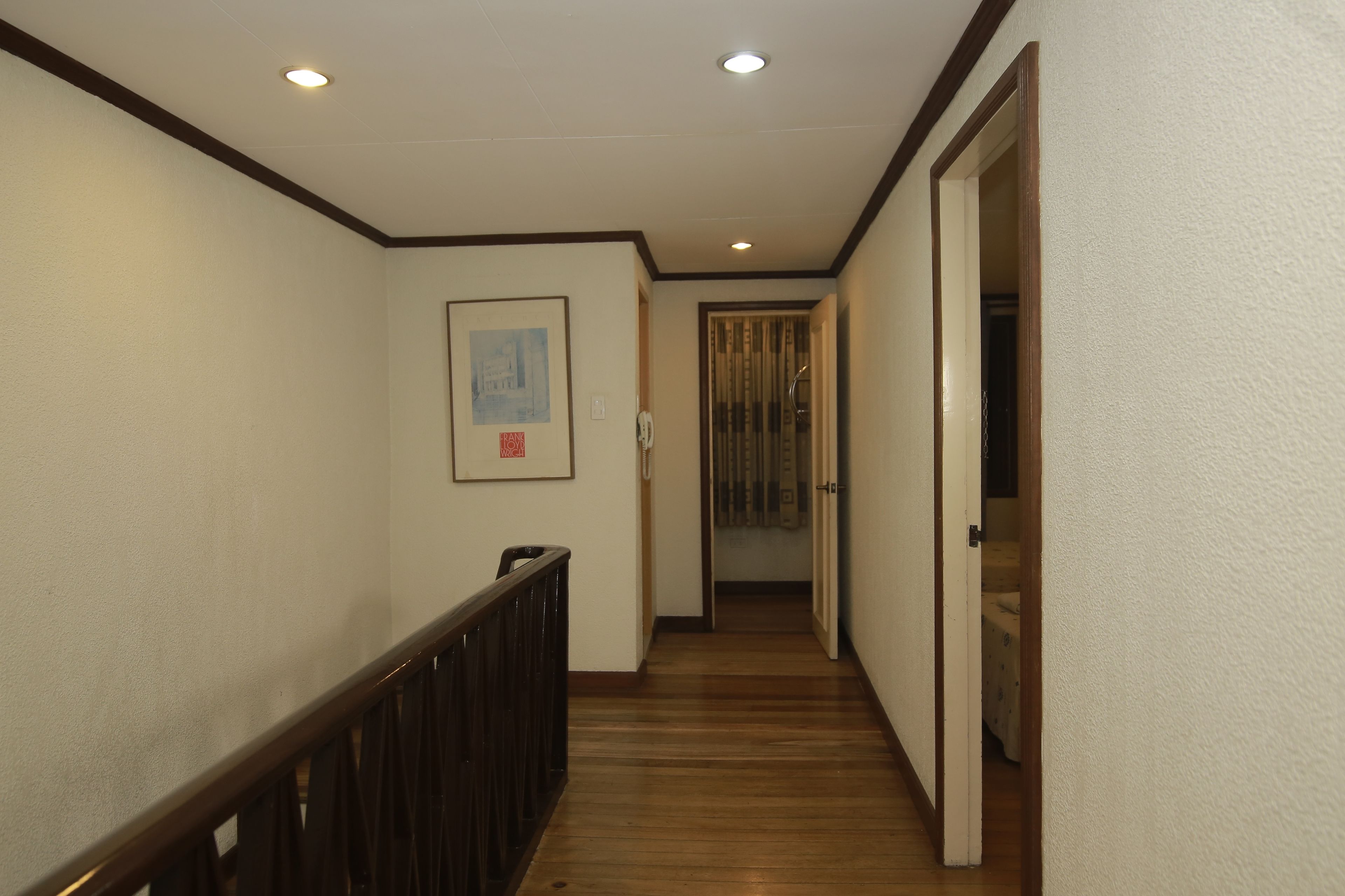 A narrow hallway with wooden flooring, white walls, and a dark wooden railing.