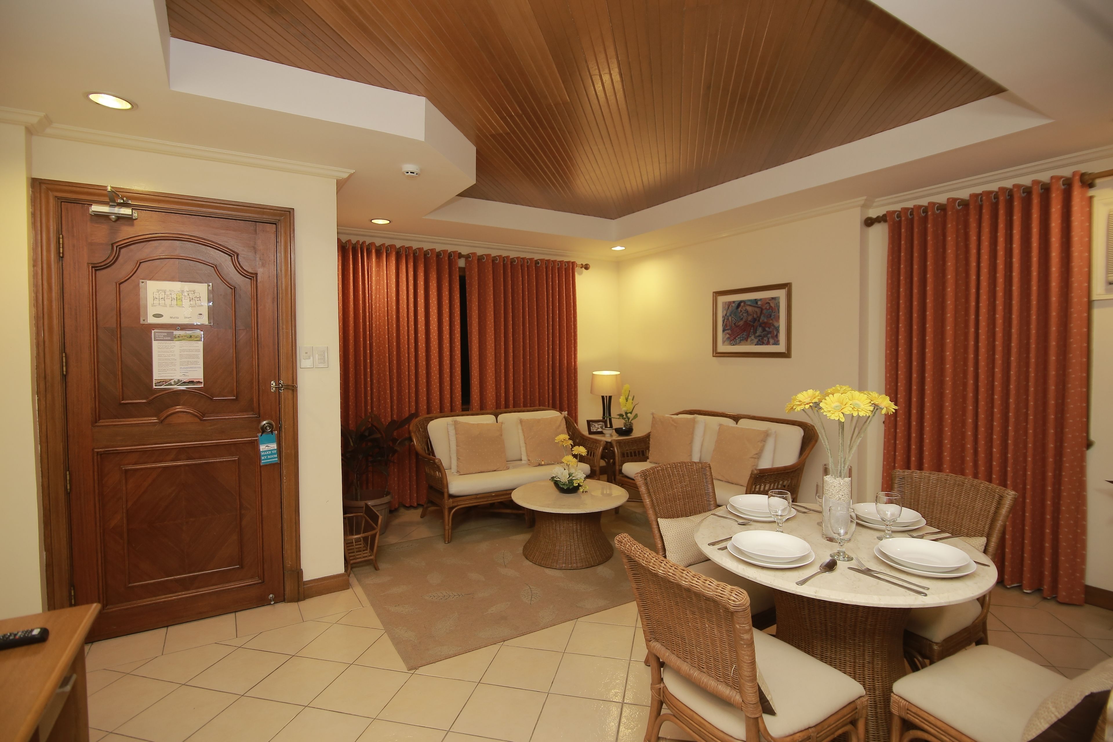 A hotel room with a dining area, a sofa set, a wooden ceiling, and a door with a notice.