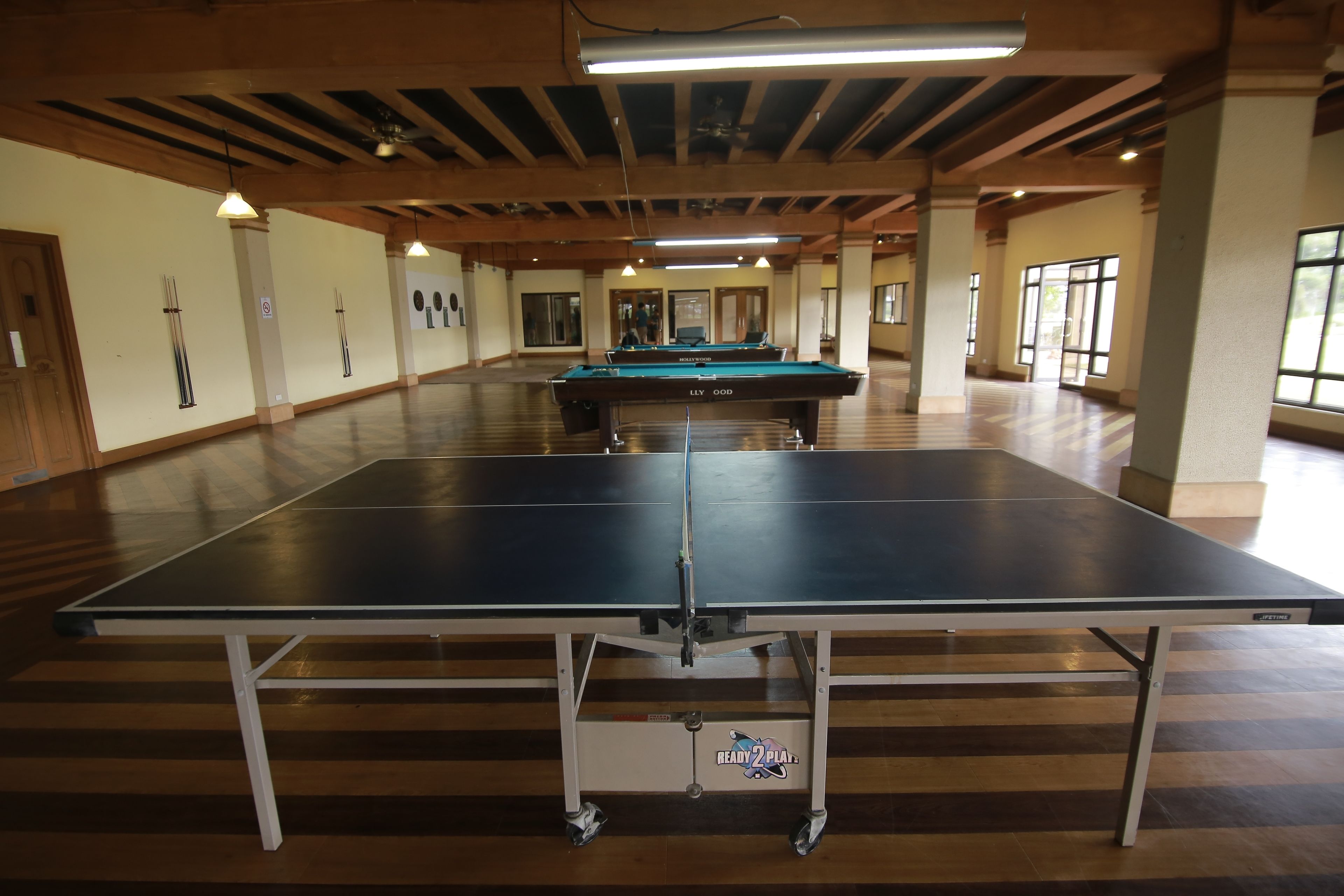 Amplio espacio interior con mesa de billar y mesa de ping pong, pisos de madera y ventanas grandes.