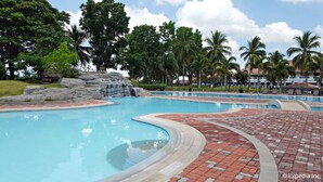 A large outdoor swimming pool with a waterfall feature, surrounded by palm trees and a rocky landscape. - The Suites at Mount Malarayat (Lipa)