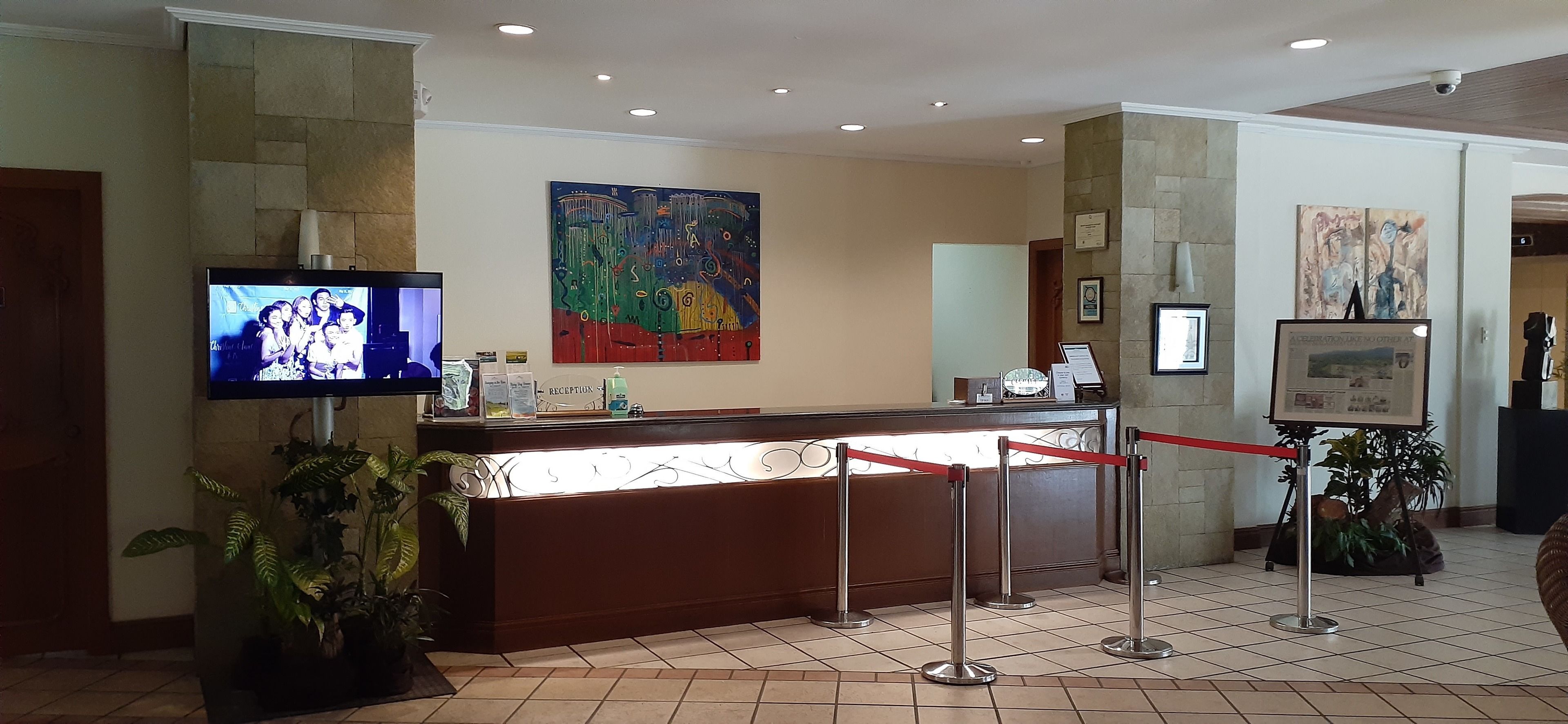 Un espace d’accueil avec un comptoir, un téléviseur affichant une photo de famille, un tableau abstrait aux couleurs vives et un certificat encadré accroché au mur.