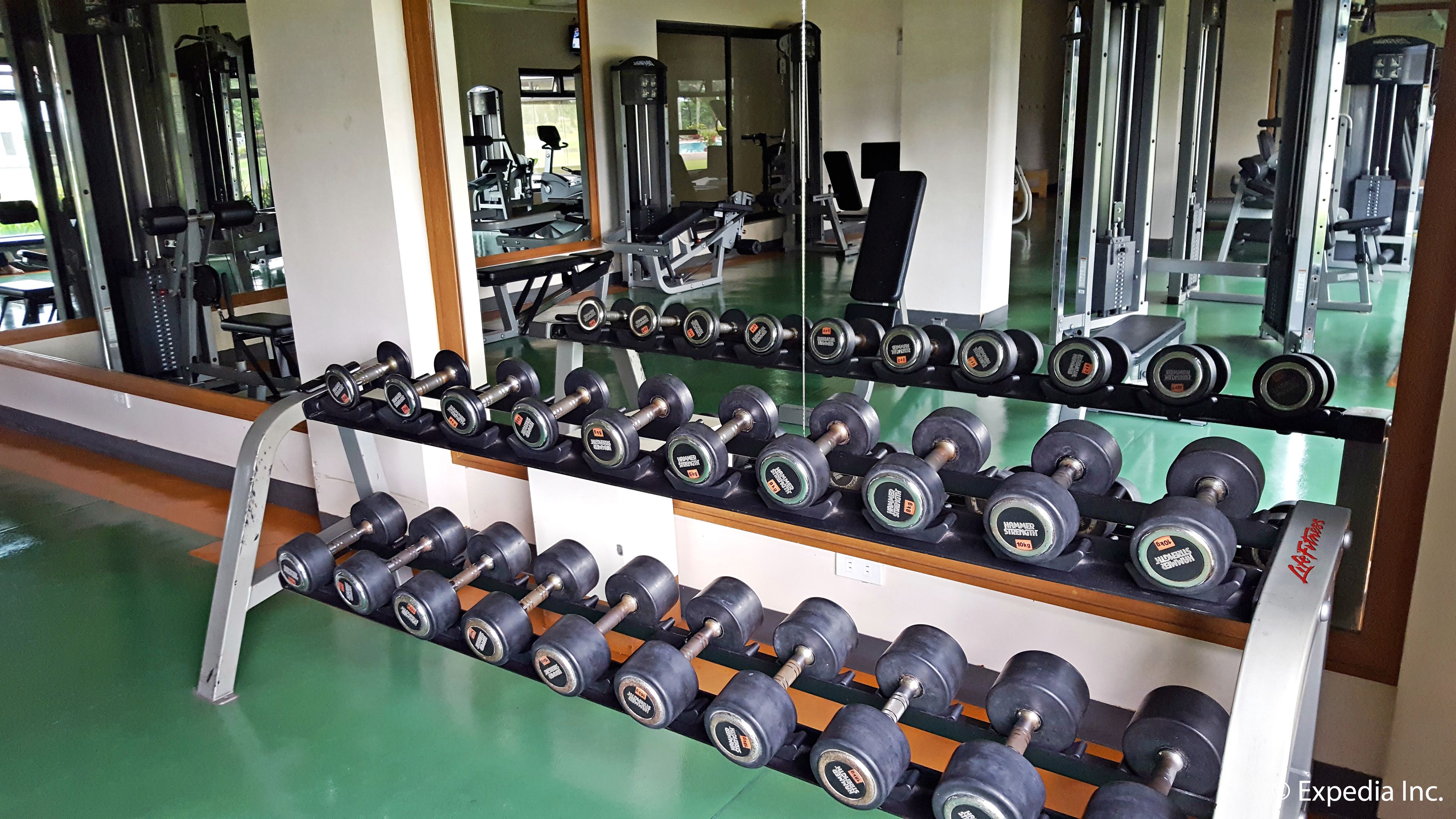 A gym with rows of dumbbells on racks, mirrors on the walls, and various exercise machines.