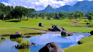A golf course with a pond, palm trees, and mountains in the background. - The Suites at Mount Malarayat (Lipa)