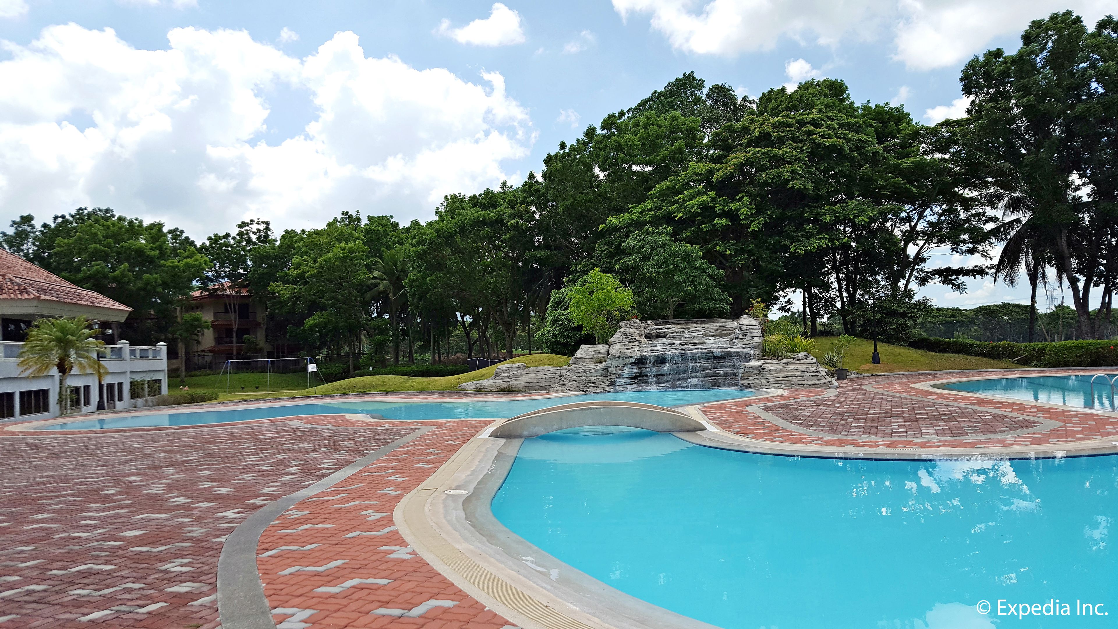 A swimming pool with a waterfall feature, surrounded by a brick pathway and lush greenery.