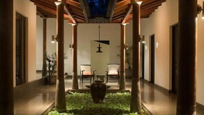 Un pasillo con un jardín central, pilares de madera y una lámpara colgante.