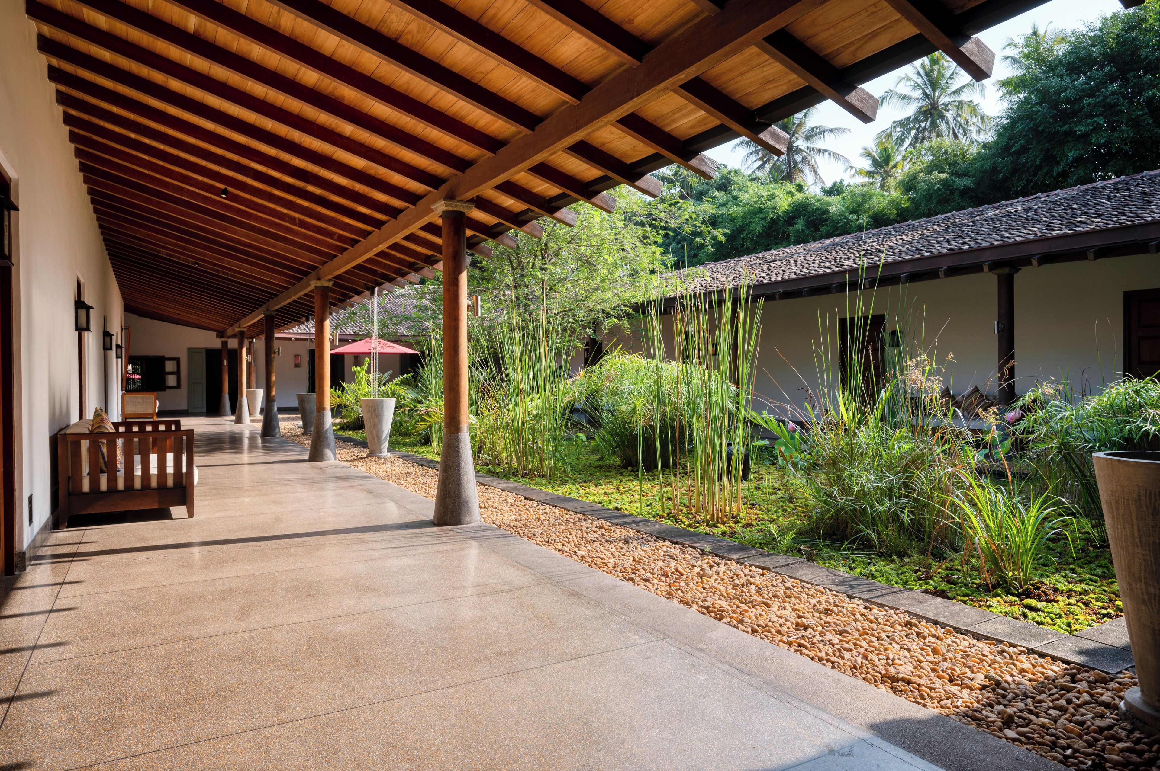 A covered outdoor area with a bench, potted plants, and a pathway leading to a building.
