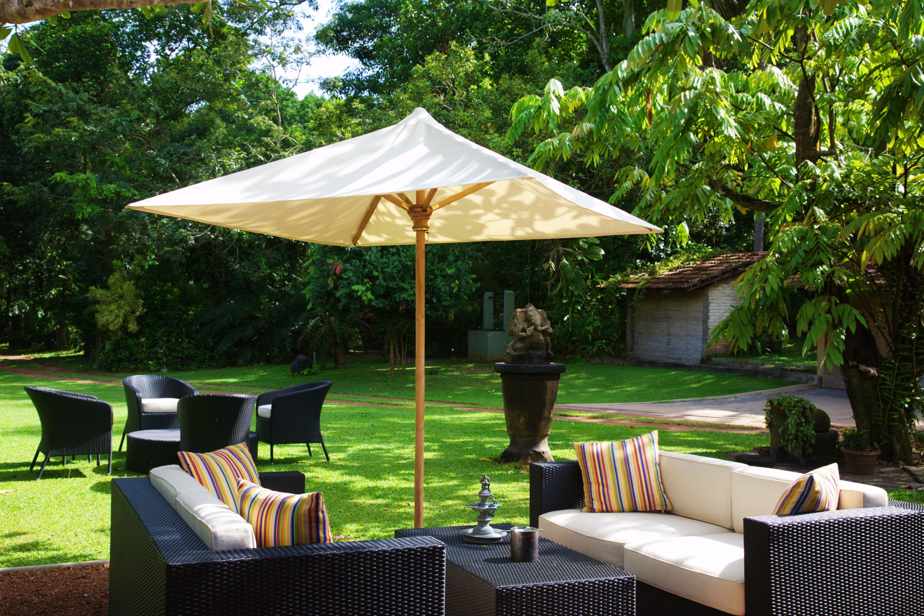 An outdoor seating area with wicker furniture, a white umbrella, and lush greenery.