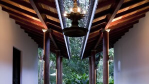 Un pasillo con techo de madera, una fuente central y vistas al exterior con vegetación.