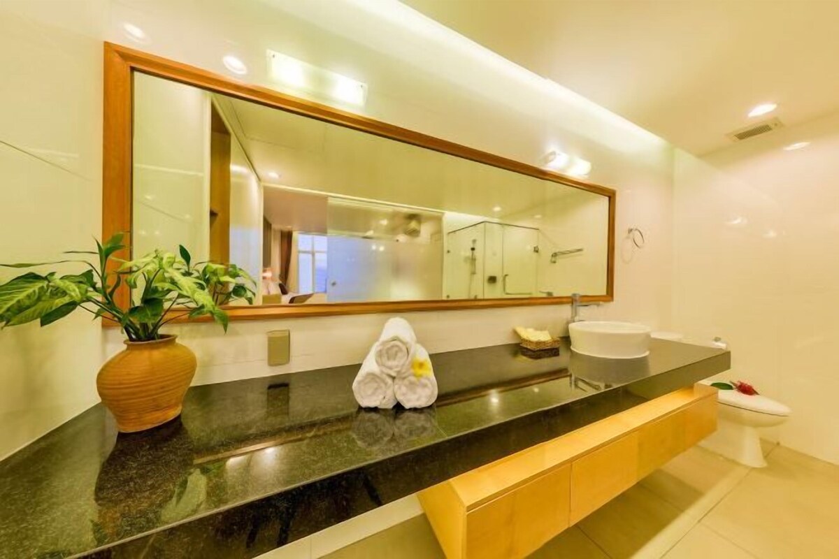 A modern bathroom with a large mirror, a black countertop, a sink, a toilet, and a potted plant.