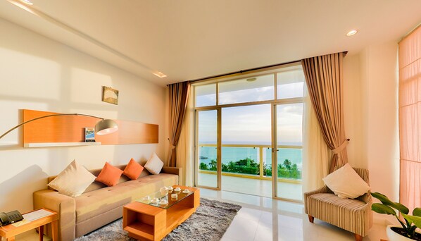 A modern living room with a sofa, coffee table, and a large window offering a view of the ocean.