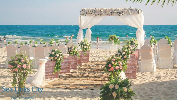 A beach wedding setup with a floral arch, white chairs, and a sandy path leading to the sea.