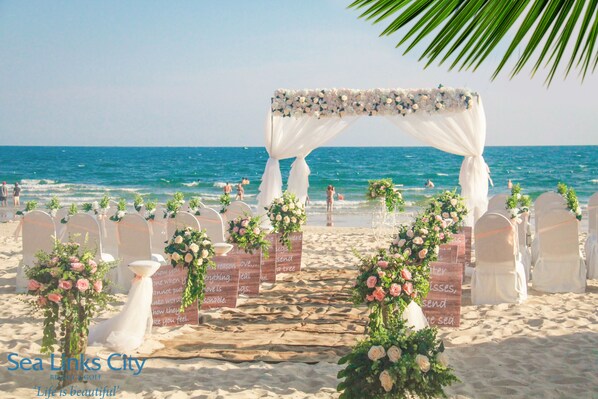 A beach wedding setup with a floral arch, white chairs, and a sandy path leading to the sea. - Ocean Vista (Phan Thiet)