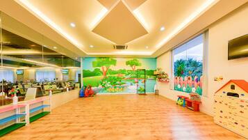 A children's play area with a mural, wooden flooring, and a TV screen in the background.