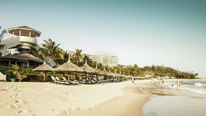 A beach with thatched umbrellas, lounge chairs, and a lifeguard tower.