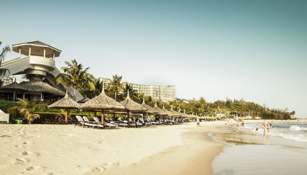 A beach with thatched umbrellas, lounge chairs, and a lifeguard tower. - Ocean Vista (Phan Thiet)