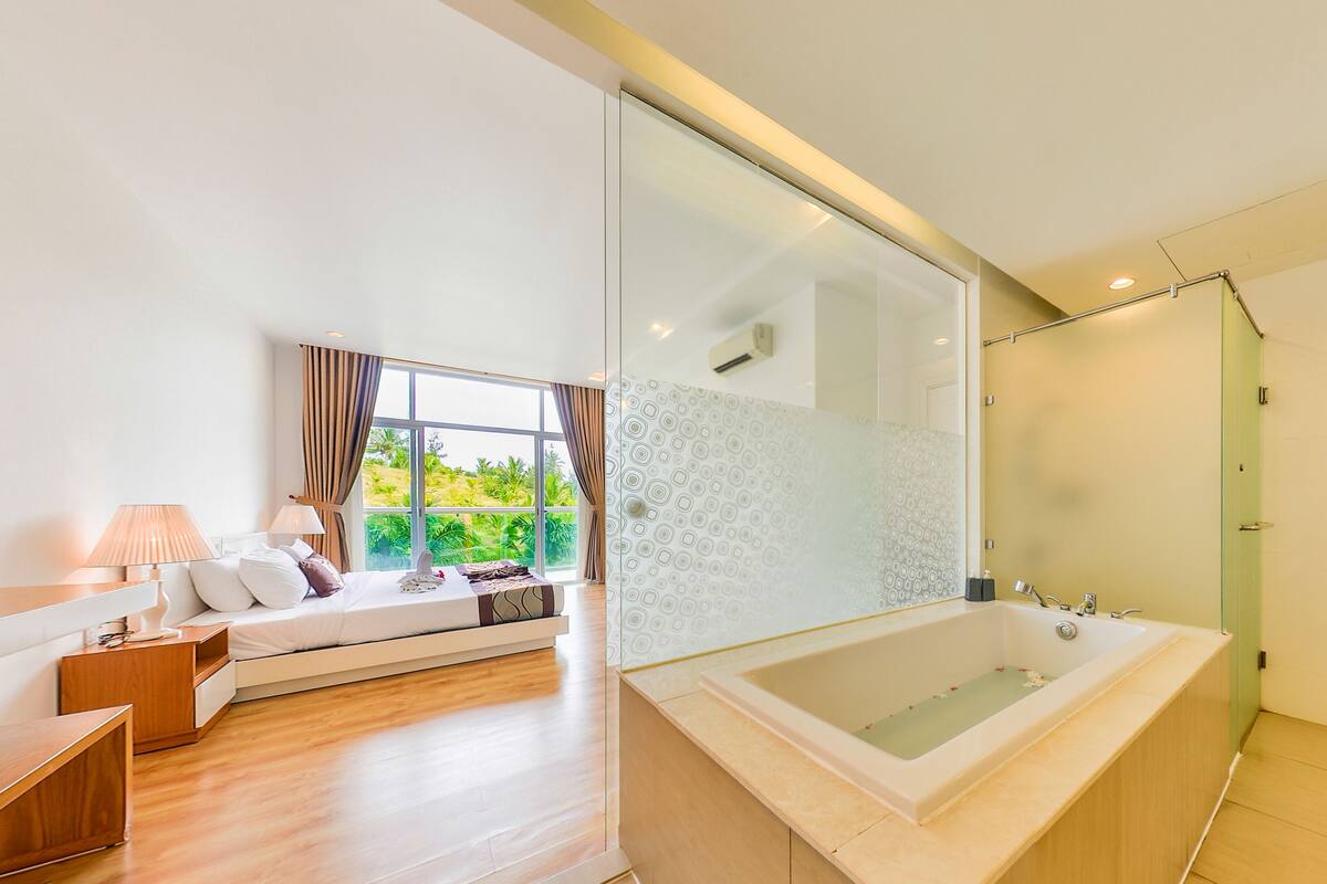 Un baño moderno con una bañera grande, cabina de ducha con mampara de vidrio y vistas al exterior.
