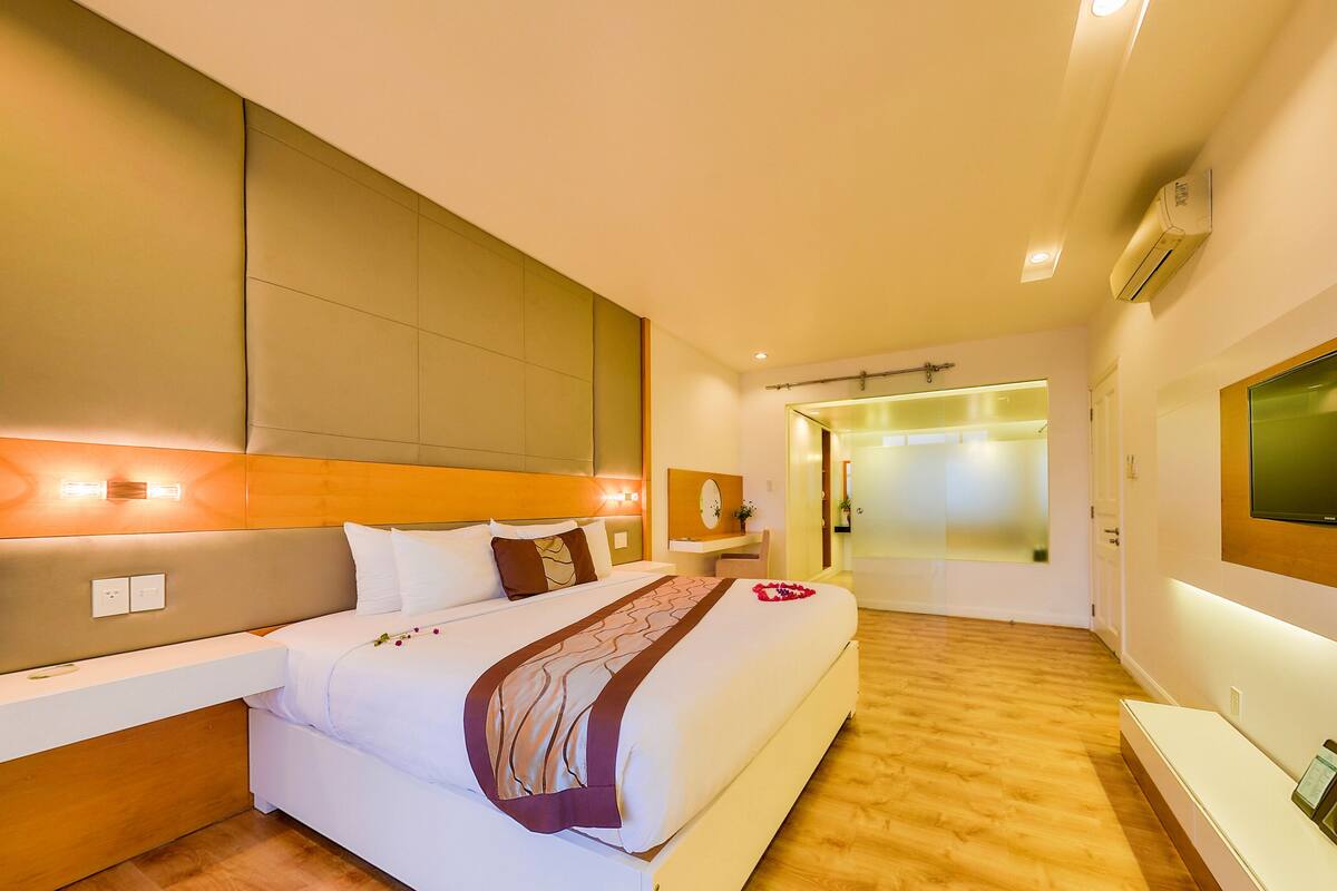 Habitación de hotel con una cama grande, un televisor montado en la pared y un baño visible a través de una puerta de cristal.