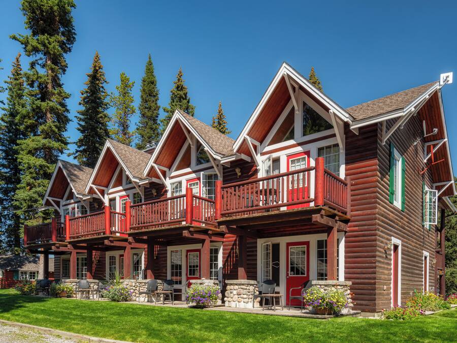 A log cabin hotel with multiple balconies, a stone foundation, and a well-maintained lawn.